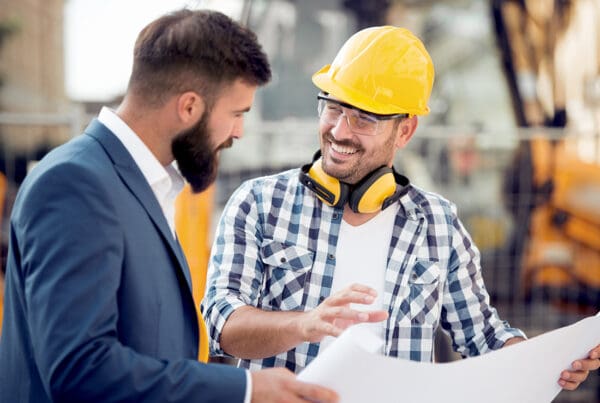 Business Insurance - Cheerful Contractor Discussing Building Blueprints with a Businessman on a Commercial Jobsite